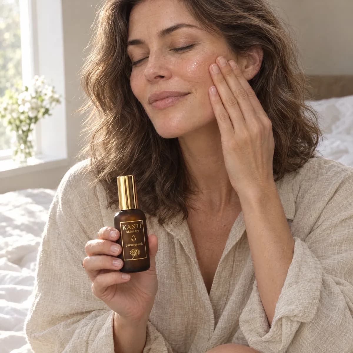 Woman pressing Kanti Paracress oil into her cheek by a sunlit bedroom window